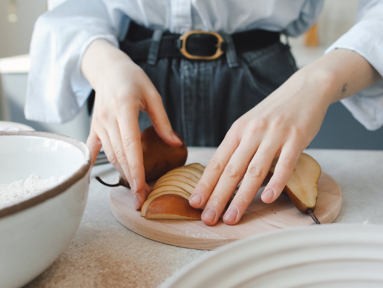 A person preparing sliced pear in a kitchen setting enhances the culinary atmosphere.