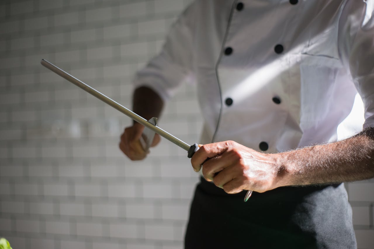 Professional chef sharpening a knife with a honing rod in a kitchen setting.